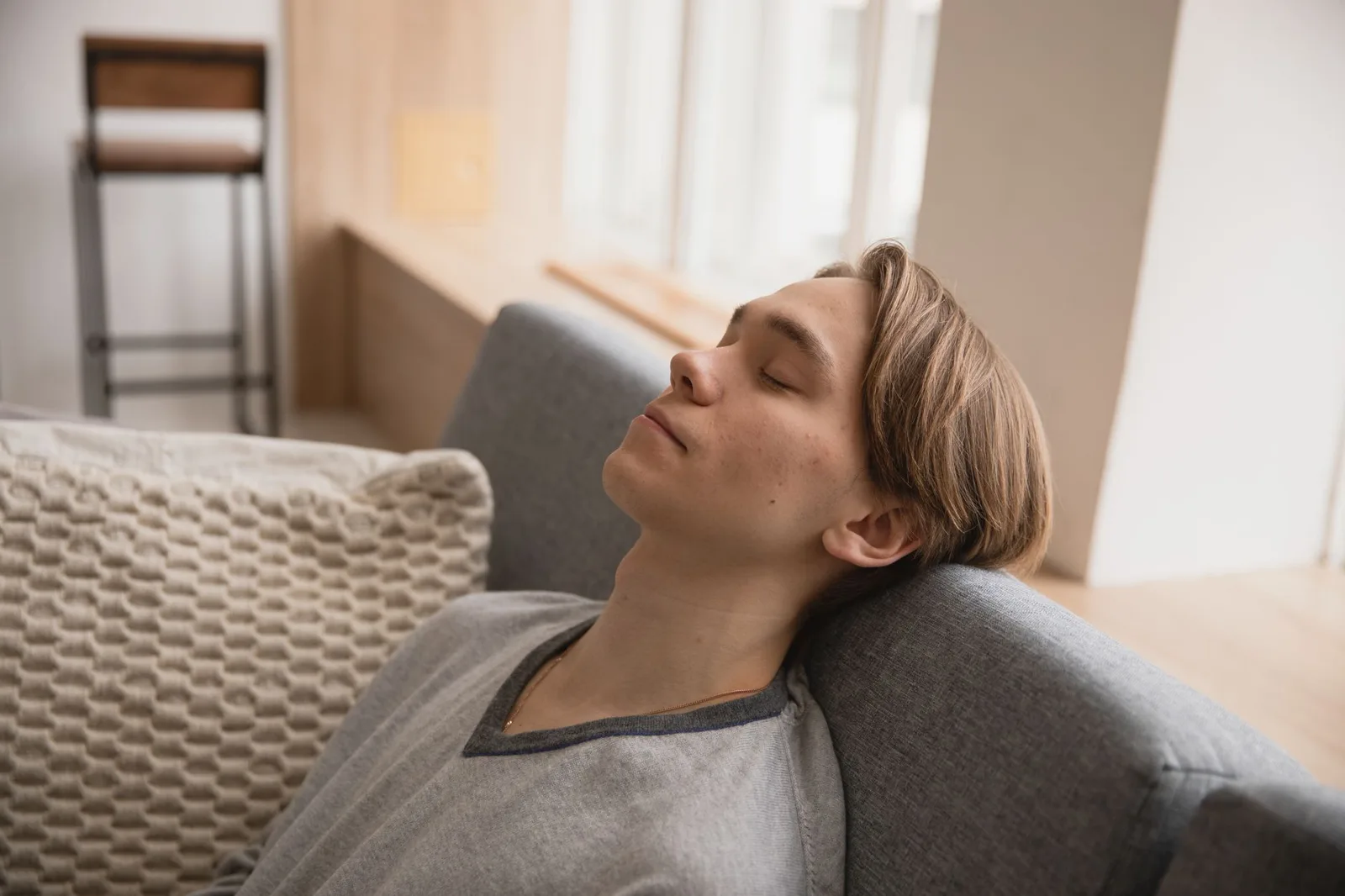 Young man resting on a grey sofa with his eyes closed